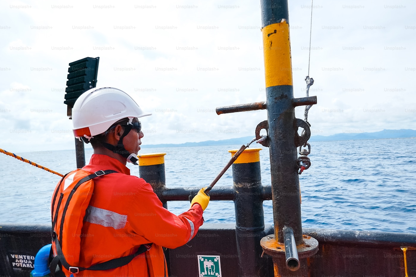 Profissional em macacão laranja e capacete de segurança em embarcação offshore no mar